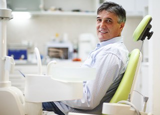 Older male patient sitting up in dental chair smiling