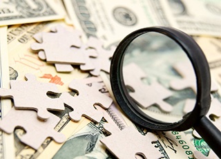 Magnifying glass resting on top of scattered puzzle pieces and money
