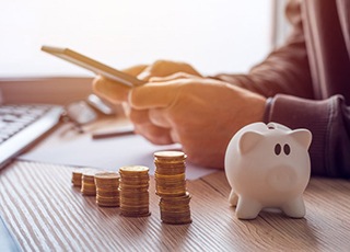 Man using a calculator at his desk with a stack of coins and a piggy bank nearby